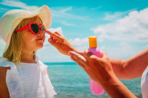 sun protection - mom put suncream on little girl face at beach vacation; blog: Sun Safety Tips for Kids