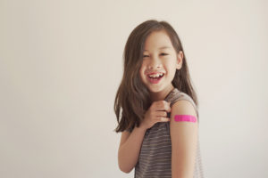 Asian young girl showing her arm with pink bandage after got vaccinated or inoculation, child immunization, covid delta vaccine concept; blog: Flu Shots for Kids